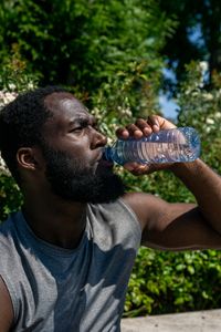 Athletic man drinking water from plastic bottle in sunny outdoor setting.