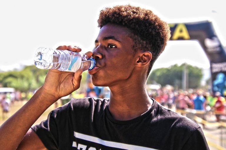 A young man drinking bottled water outdoors at a sporting event, showcasing hydration and fitness.