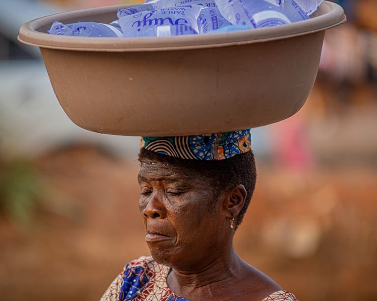An African woman in Nigeria balances a basin of sachet water on her head, showcasing local street vending.
